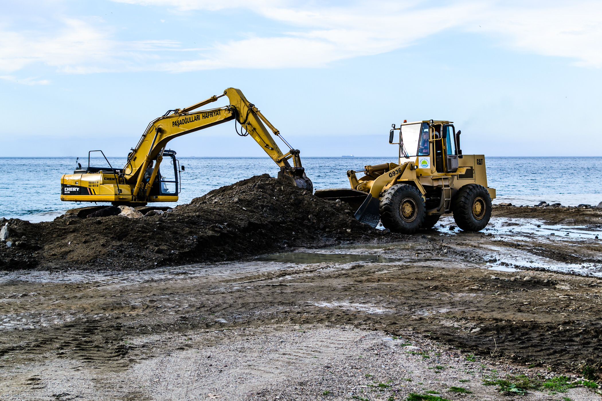 An excavator and a wheel loader working on a land reclamation project near the sea.