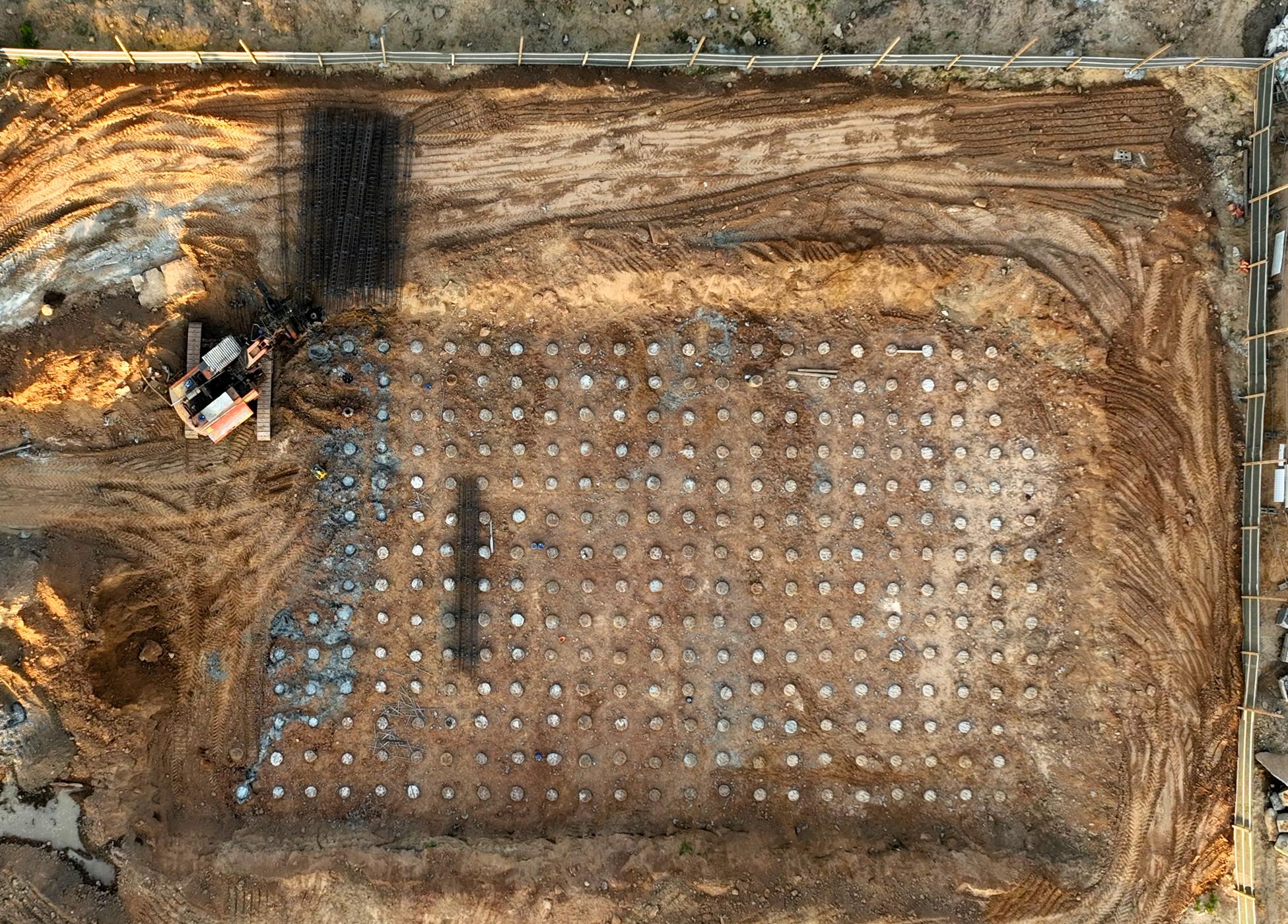 Aerial view of construction site showing deep foundation grid with drilled piles and excavation equipment.